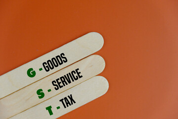 Wooden ice cream sticks with word GST. abbreviation of goods and services tax on orange background....