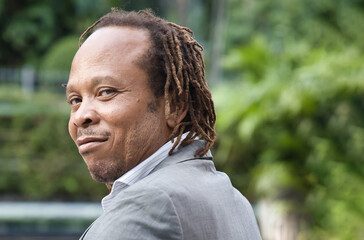 Confident, happy, smiling, positive middle aged African office worker or businessman in green park near office, looking over shoulder back at you