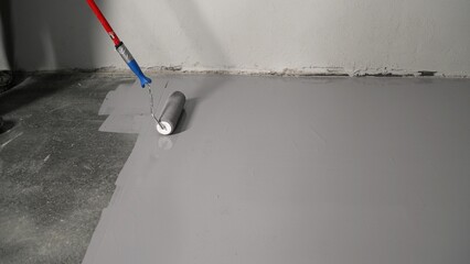 Construction worker applying epoxy coating on concrete floor using a roller