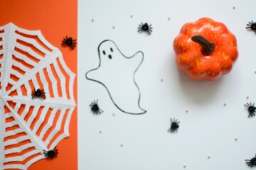Halloween composition with spiders, pumpkins, cobwebs and ghosts on an orange and white background