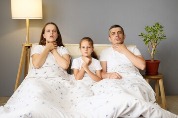 Sick father lying beside daughter and his wife with painful neck ache suffering from strong cold...