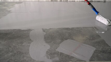 Construction worker applying epoxy coating on concrete floor using a roller.