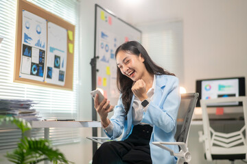 A woman is sitting at a desk with a cell phone in her hand