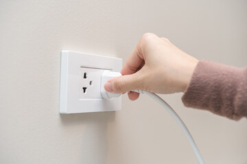 Hand of woman plugged in, unplugged electricity cord cable at home, put on or remove electric plug cable in socket on wall outlet for saving, control power electrical energy, eco environment concept.