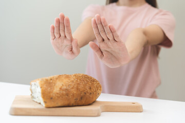 Gluten allergy, asian young woman hand push out, refusing to eat white bread loaf on board in breakfast food meal at home, girl having a stomach ache. Gluten intolerant and Gluten free diet concept.