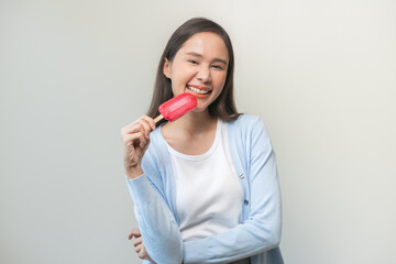 Cheerful, happy positive asian woman wearing casual with brunette hair, enjoy eating delicious popsicle, girl holding cold dessert, frozen stick with strawberry ice cream tasty isolated on background.