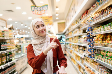 Happy mature Asian woman looking  products at grocery store. Costumer buying food at the market. Woman enjoying her time shopping at the grocery store