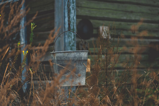 A bucket hangs on a chain against the background of an old, rustic house