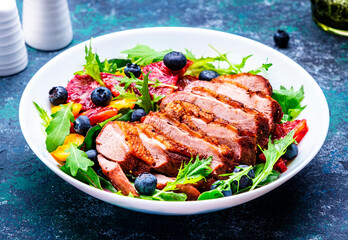 Foodie food salad with grilled duck and bloody orange, kumquat, blueberry and lettuce on blue background, top view
