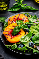Vegan delicious salad with grilled peaches, fresh blueberries, red onion, walnuts, basil and mixed herbs, black background, top view
