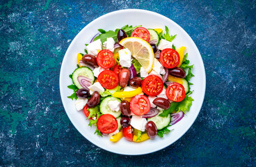 Traditional greek salad with feta cheese, kalamata olives, tomatoes, paprika, cucumber and onion, healthy mediterranean diet food. Blue table background, top view