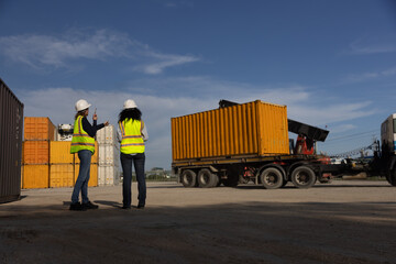 Two women logistics engineers supervise the loading of goods at a container yard for overseas...