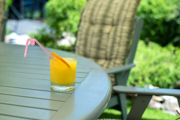 a glass of orange juice on a table in the garden.