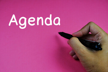 hand holding a pen with text of Agenda for today meeting on pink background 