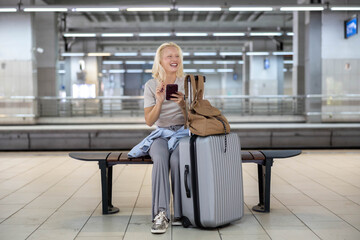 A woman traveler comfortably seated on a public bench, interacting with her smartphone, is spotted...