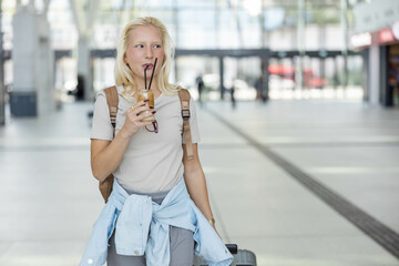 A traveler with a suitcase and backpack enjoys iced coffee at an railway station, embodying themes...