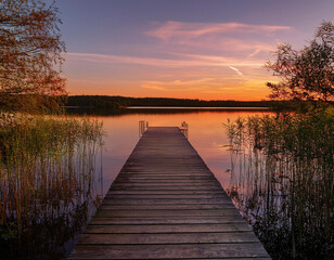 Obraz premium A serene wooden jetty stretches over a tranquil lake at sunset