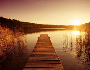 Obraz premium A serene wooden jetty stretches over a tranquil lake at sunsetin in a warm golden glow