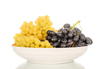 Two bunches of ripe white and black grapes in a ceramic dish, macro, isolated on white background.