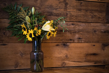 A vibrant bouquet of sunflowers, lilies, and greenery in a glass vase, set against a rustic wooden backdrop. The floral arrangement highlights natural beauty in a simple yet elegant setting.