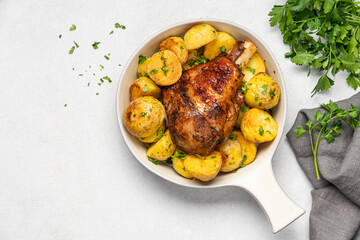 Baked golden turkey leg with potatoes in ceramic dish on light table with copy space
