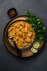 Chicken curry in black bowl with green herbs and lime on  dark background with copy space. Traditional asian food