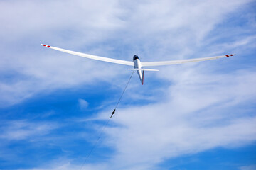 a white glider is pulled up steeply into the sky by a wind in a sunny sky
