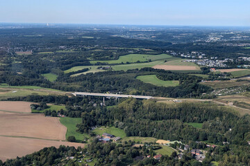 Obraz premium view from above of the fields, forests and highway bridge angertal A44 with heiligenhaus in the background on a sunny day