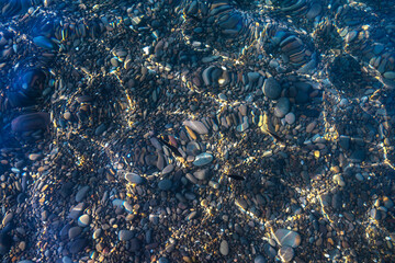  Underwater pebble backgrounds. Colorful stones sea bottom and sea fish in the sun rays. View from above through clear water. Seascape wallpaper texture.