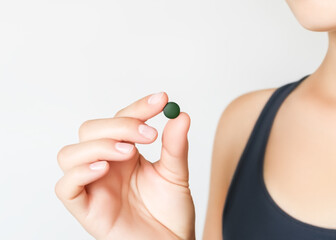 hand holding green chlorella and spirulina pill on grey background