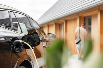 Young man plugging a charger in electric car at modern house home