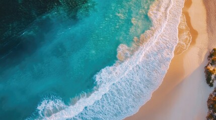 Aerial shot of a serene blue sea with gentle waves and a bright sandy beach, all under sunny weather