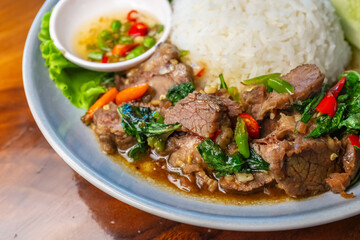 Closeup Stir-fried beef with basil in a blue plate with fish sauce, chili, cucumber and lettuce on a wooden table.