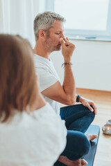 A man sitting in lotus position and a woman practicing alternate nostril breathing exercises during...