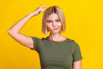 Photo of suspicious puzzled girl with bob hairstyle dressed khaki t-shirt finger scratching head isolated on yellow color background