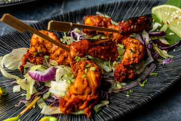 Chicken tandoori with sliced onion and cabbage served on a decorated plate with lemon piece and stick