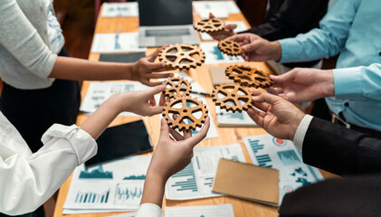 Group of multiracial business people joining gear wheels together over table as effective unity and productive teamwork concept. Efficient system business team process for solution solving. Meticulous