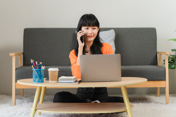 Focused Young Woman Working Remotely: A young Asian woman sits comfortably on the floor, engrossed...