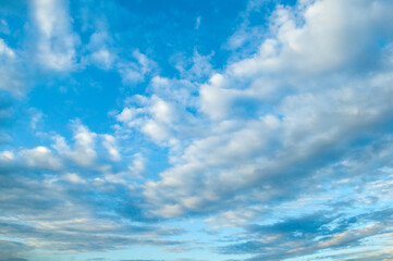 Cloudy blue sky with fluffy clouds lit by sunlight - natural cloudy sky background, panoramic view of blue cloudy sky
