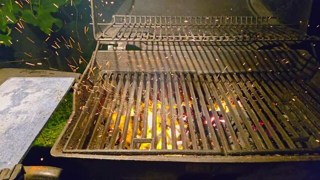 The fire burns through the grill grate. Coal for barbecue prepared by blowing the firewood. BBQ fire hearth spiting ambers in the air in slow motion.BBQ grill with bright glowing flames.