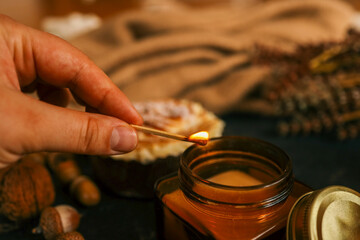 Close-up of a person lighting a scented candle with a matchstick, creating a warm and cozy ambiance, perfect for a relaxing evening