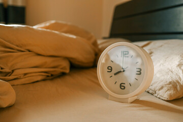 A white alarm clock lies on a soft beige blanket, creating an atmosphere of coziness and morning...