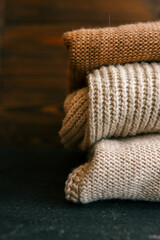 Close-up of folded knitted sweaters in neutral tones on a dark surface. Perfect for concepts of warmth, coziness, fashion, and autumn or winter seasons