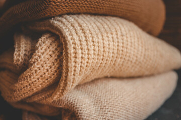 Close-up of folded knitted sweaters in neutral tones on a dark surface. Perfect for concepts of warmth, coziness, fashion, and autumn or winter seasons
