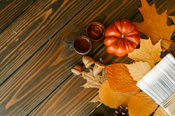 Top view of a paintbrush placed on dried autumn leaves with acorns, pine cones, and a pumpkin on a...