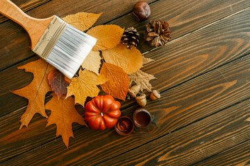 Top view of a paintbrush placed on dried autumn leaves with acorns, pine cones, and a pumpkin on a...