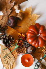 Autumn flat lay with leaves, pine cones, acorns, mini pumpkin, and candles arranged on a light background for seasonal decoration