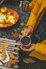 Children in warm clothing holding cups of hot drink near a bonfire in the evening. Cozy autumn outdoor scene with a fire pit, fallen leaves, and rustic snacks, capturing the essence of fall warmth