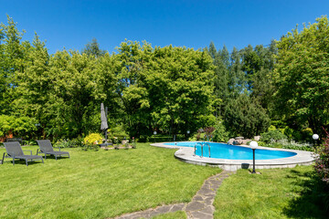 Swimming pool with sun beds on a closed private territory on a clear sunny day. Dense .greenery...