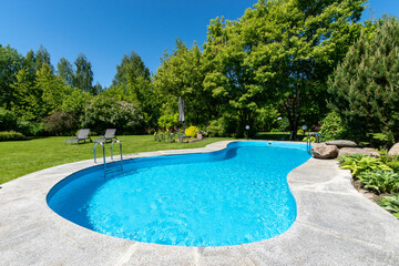 Outdoor private swimming pool against the blue sky, surrounded by green shrubs.